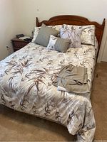 Full view of full size bed with headboard, patterned bedding, and matching wooden nightstand.