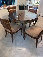 Overview of round glass top table with four matching chairs arranged around it on tiled floor.