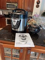 Power Pressure Cooker XL Pro electric pressure cooker along with black ceramic vase and instruction manual shown on kitchen countertop.