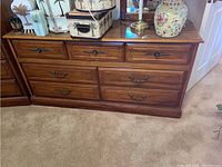 Photo of the front left side of the wooden 7 drawer dresser with decorative metal handles and polished finish. Shows three top small drawers and four larger drawers below.