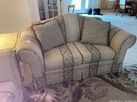 Full view of the Bassett loveseat in a living area, showing the rolled arms, skirted base, and two square pillows.