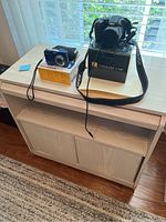 Nikon Coolpix L340 and Kodak EasyShare CD82 cameras displayed on top of light wood storage cabinet with two sliding doors and two open shelves