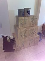 Stacked painted storage boxes with floral design and two metal cat figures on the floor beside them