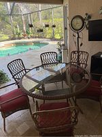 Photo showing round glass top bamboo style patio table and six metal chairs with red cushions in screened outdoor patio area.