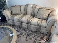 Full view of Bassett beige fabric sofa with decorative pillows on a floral area rug.