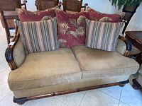 Front view of beige Cindy Crawford loveseat with five decorative pillows on tiled floor.