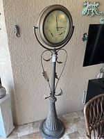 Full view of the tall metal standing clock showing spotlight style design, base, and decorative metal leaves.