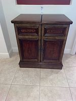 Front view of solid wood mini bar with closed folding top, ornate carved panels on doors and drawers.