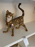 Image of a standing ceramic cat sculpture with striped patttern and smiling face. Visible tag attached to collar and small marks on tail.
