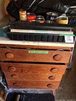 Wooden drawers cabinet holding assorted tools with cans and trays on top.