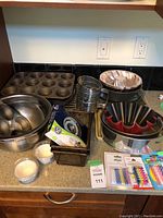Overview of baking items including muffin tins, mixing bowls, metal ring molds, Bundt pans, cupcake liners, candles, and racks.