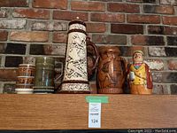 Front view of five assorted beer steins on a ledge showing variety of designs and materials