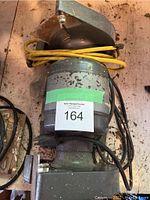 Top-down photo of the bench grinder showing motor casing, power cord wrapped on top, and grinding wheels. Shows surface wear and dirt on metal parts.