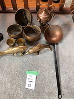 Full overview of the brass and metal lot showing hanging pots, kettle, fish and dolphin ornaments, and long handled pan.