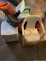 Photo of white VIP 12L portable toilet with child chair, cooler bag, orange tent bag, and other camping gear.