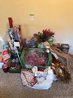 Wide view of Christmas items including gift wrap, wreath, centerpiece, candle holders and more arranged on floor.