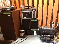 Wide view showing all items including Sony large speakers, Centrios speakers, Teac cassette deck, GE radios, Sony Handycam, and Kodak camera