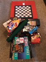 View of stacked board games and card game accessories, showing the roll-up card table mat, board games, multiple decks of cards, and poker chips on carpet.