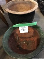 Two garden pots stacked, large black pot at the back and smaller green-rimmed clay pot in front with seller's lot tag.