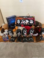 Shows a collection of toys including plush stuffed animals, KISS bobbleheads, Itty Bitty KISS figures in a box, and a Kermit talking toy.