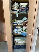 Closet shelf with stacked linens including blankets, towels, and cloths in different colors and patterns