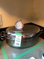 Large metal roasting pan with lid and oven thermometer on top
