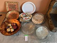 Assorted serving trays and dishes with a wooden fruit bowl containing faux fruit in used condition