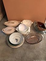Various serving bowls and dishes arranged on carpeted floor, including ceramic and glass items, some with lids or handles.