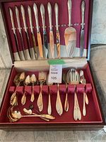 Open wooden canteen displaying the full silverware set arranged neatly inside on red velvet lining. 8 dinner knives, forks, teaspoons, tablespoons, and large serving utensils visible.
