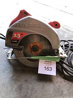 Photo showing front and top part of the Skilsaw circular saw with visible blade guard, power specs sticker, and power cord in coiled state.