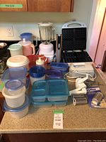 Full lot showing blender, waffle maker, assorted plastic containers, hand mixer, cheese grater, electric corkscrew on counter