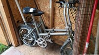 Two silver folding bicycles side by side against OSB wall