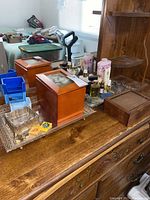 Wide angled photo showing the wooden dresser surface with perfume bottles, large and small wooden boxes, some watches, and blue plastic organizer bins.