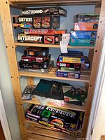 Shelf of vintage board games and electronic puzzles including Mastermind, Simon, Password, Electronic Intercept, various puzzles, and a Kawasaki keyboard toy.