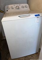 White GE top load washing machine from a front angle showing overall machine and lid
