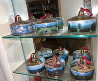 Two glass shelves with eight round Hummel music boxes, each with a brass bell and painted scenic designs