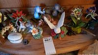 Group photo of all fourteen Lenox porcelain figurines and trinket box arranged on a wooden shelf. Various floral and animal shapes.