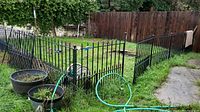 Photo showing multiple black metal fence panels installed around a grassy yard area with garden pots and hose nearby.