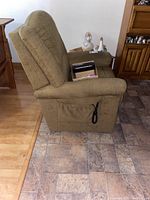 Side view of olive green Lazy Boy recliner showing padded armrest and attached remote control with black cord hanging from side pocket.