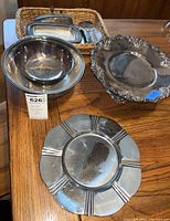 Overall view of six silver and silverplate serveware pieces including bowls, butter dish, cake stand, and serving plate arranged on wood table.