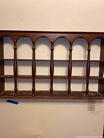 Full view of the wall-mounted wooden collectibles display shelf with detailed spindled columns and three horizontal shelves.
