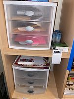 Plastic three-drawer storage units stacked on wooden shelving showing the drawers and some contents