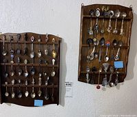 Two wooden display racks mounted on wall loaded with collectible silver souvenir spoons from around the world.
