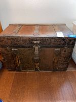Front view of wooden steamer trunk showing metal hinges, lock area, and aged wood with patina and rust spots.