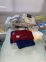 Overall view of various folded towels in multiple colors and linens on a bed, showing the quantity and condition.