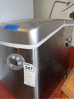 Side view of silver Whynter ice maker showing digital control panel and MaxSold sticker with dimensions taped on top.