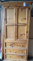 Front view of wooden cabinet showing four panel doors and three drawers with round wooden knobs.