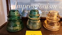 Three glass electrical power insulators in green and amber colors showing age and patina