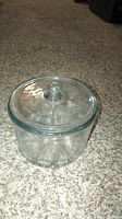 Clear glass cylindrical container with lid and knob, placed on carpet.