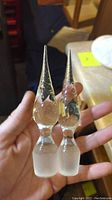 Two pointed glass vase stoppers held in hand for scale, detailed image showing texture and frosted bases.